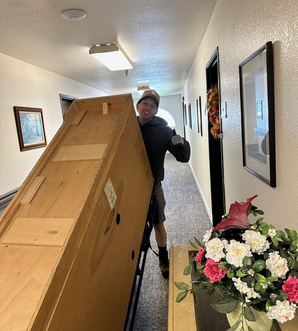 Crew member carrying a large wooden cabinet out of a house